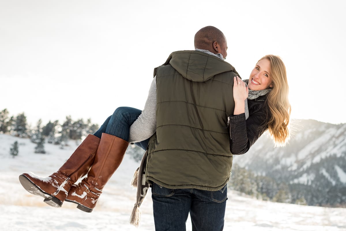 Full-length engaged couple portrait in winter mountain landscape at golden hour with perfect natural lighting