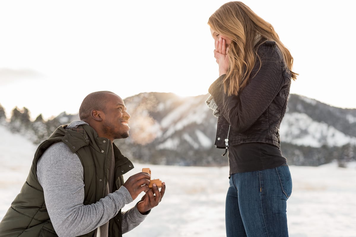 Brandon getting down on one knee during surprise winter proposal at snowy Chautauqua Park with flatirons in background