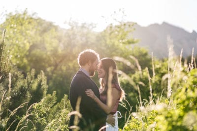 A couple looks into each other's eyes, standing in a mountain landscape