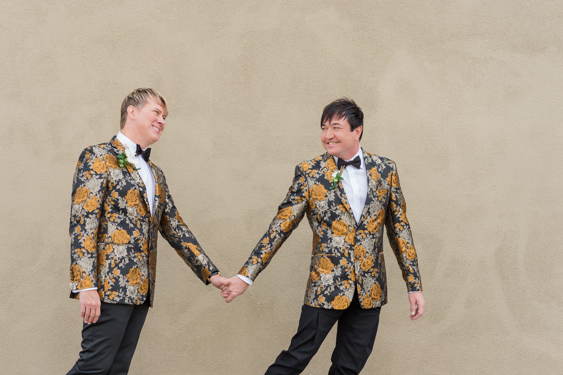 Stylish couple in colorful suits holding hands and smiling during their elopement celebration
