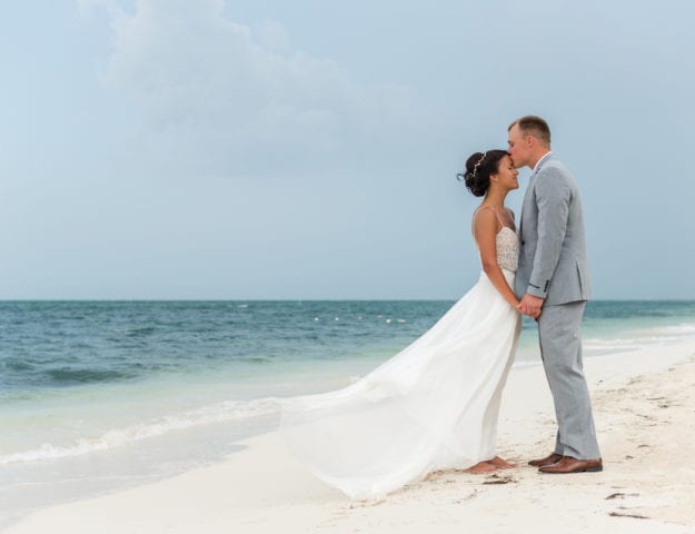 Groom kisses bride's forehead on beach