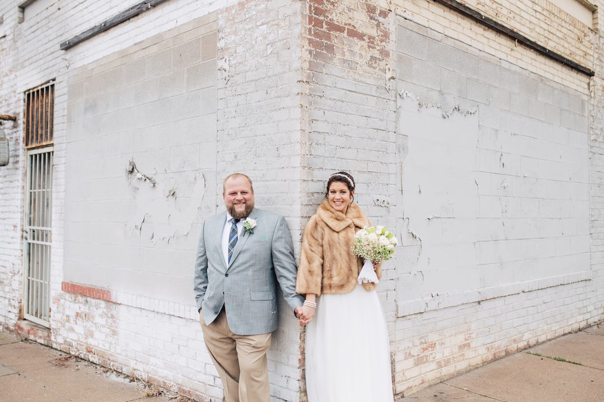 keep warm during a winter wedding | Wedding Photography | From the Hip Photo | Bride and groom stand on brick wall. Bride is wearing a fur jacket