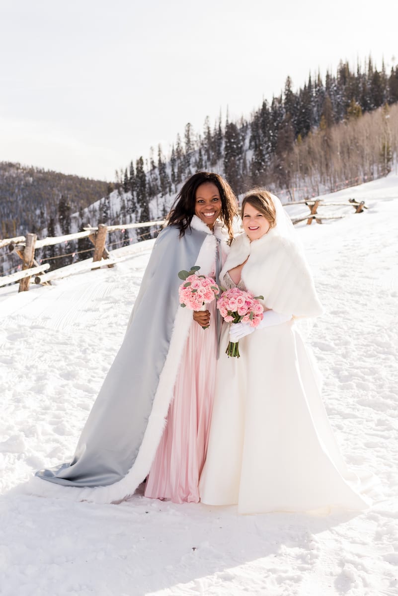 keep warm during a winter wedding | Wedding Photography | From the Hip Photo | bride and bridesmaid wear winter cloaks on snowy mountainside