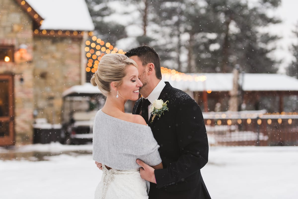 keep warm during a winter wedding | Wedding Photography | From the Hip Photo | Bride wears a light shawl while receiving a kiss on the cheek from groom