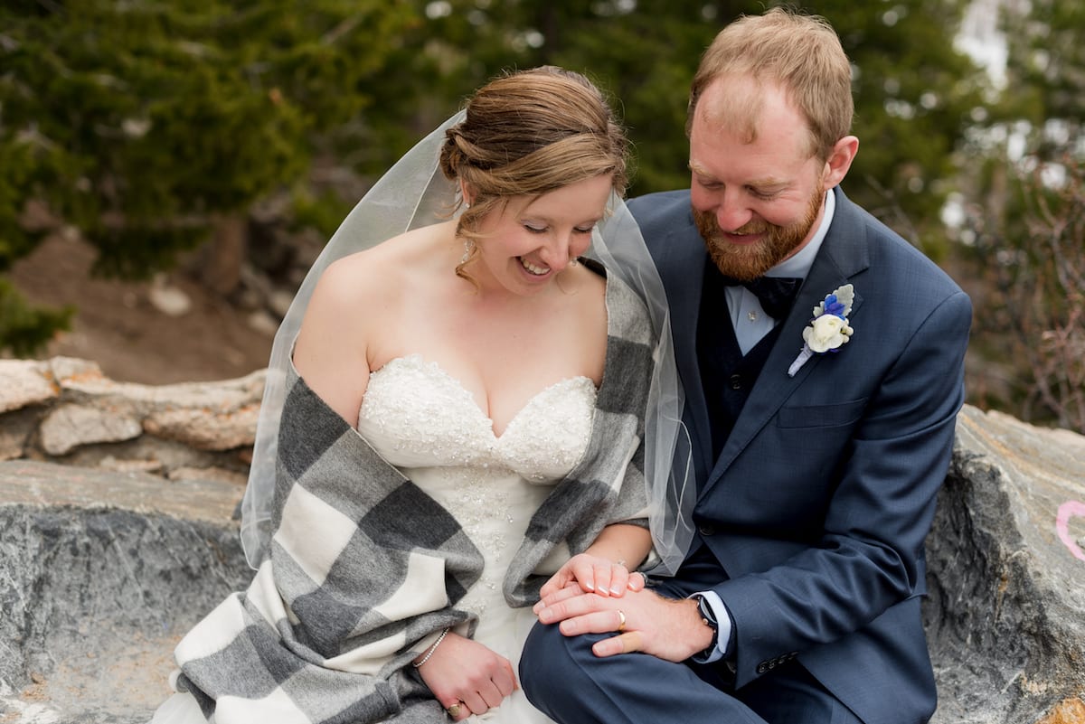 keep warm during a winter wedding | Wedding Photography | From the Hip Photo | Bride sits with groom wrapped in a gray flannel blanket
