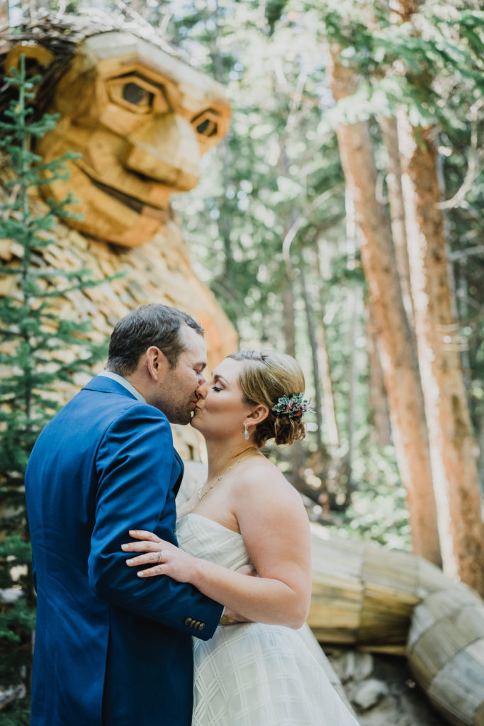Bride and groom in kiss in view of wooden troll mountain sculpture
