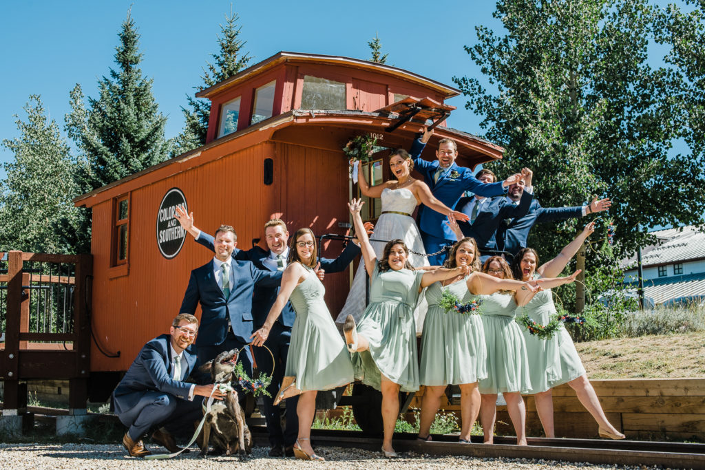 Bride and groom hand off caboose while bridesmaids and groomsmen pose around them