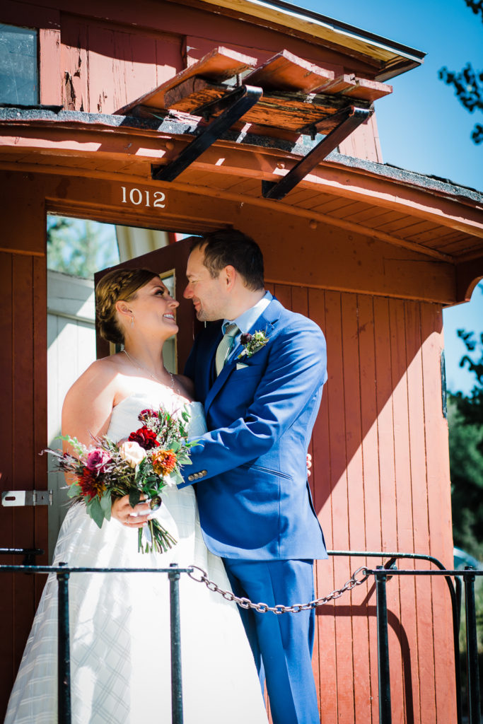 Bride and groom stand on caboose and gaze lovingly at each other