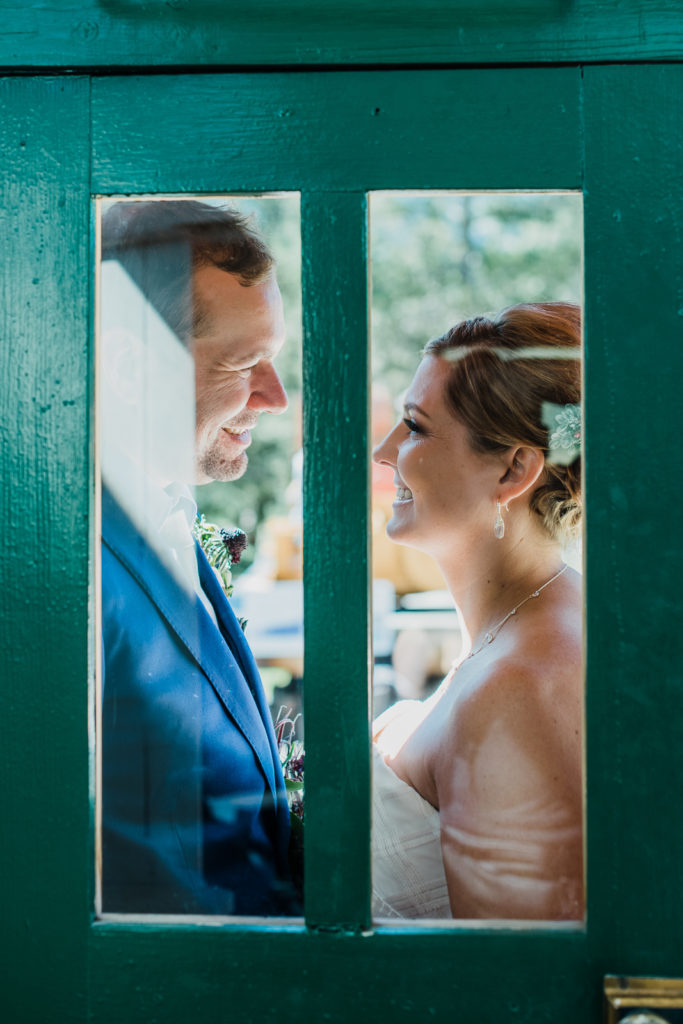 Bride and groom smile at each other behind glass panels in green door