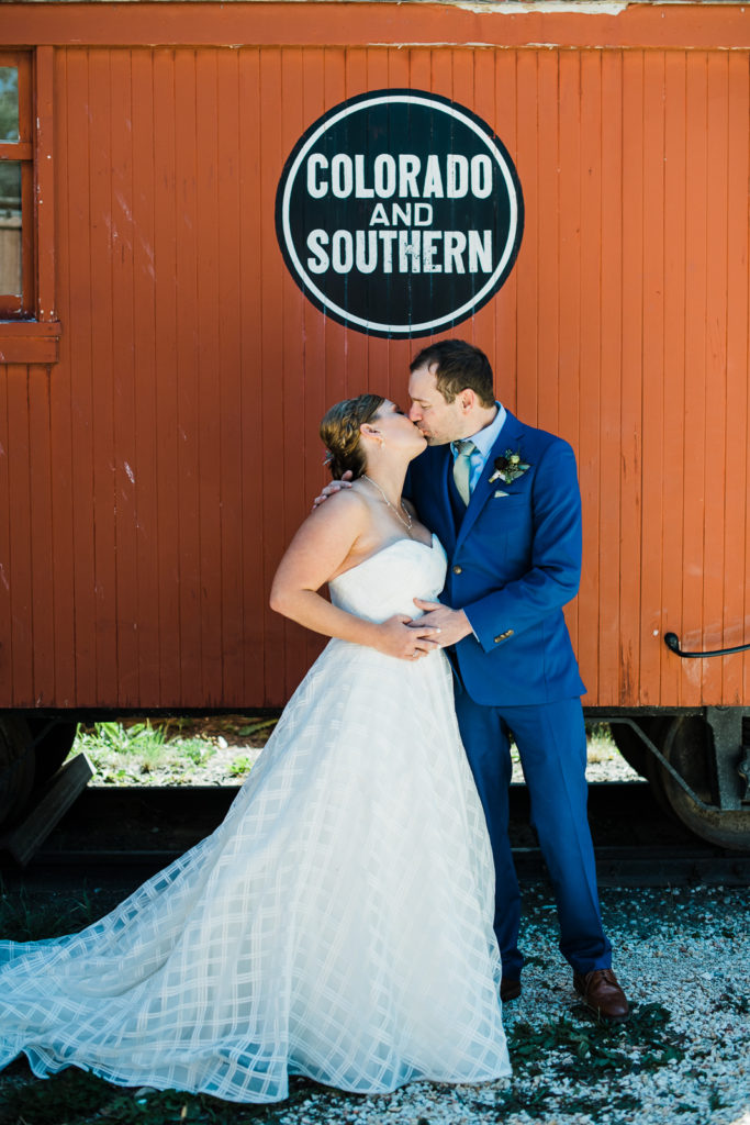 Mountain wedding in Frisco | Bride and groom kiss beneath "Colorado and Southern" banner on orange train car