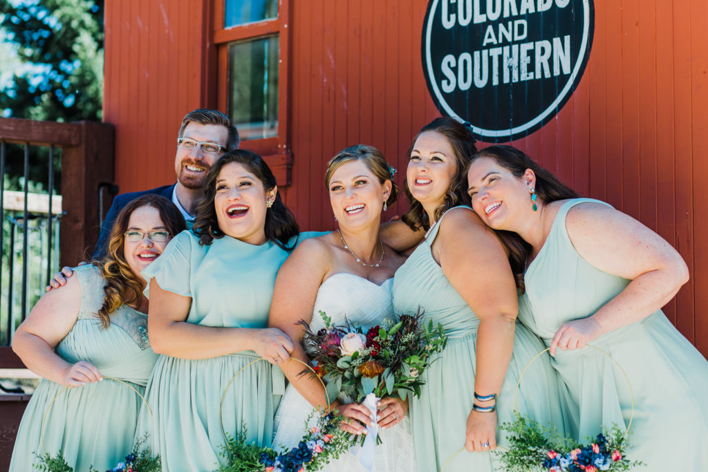 Bridesmaids and one groomsman lean close to laughing bride