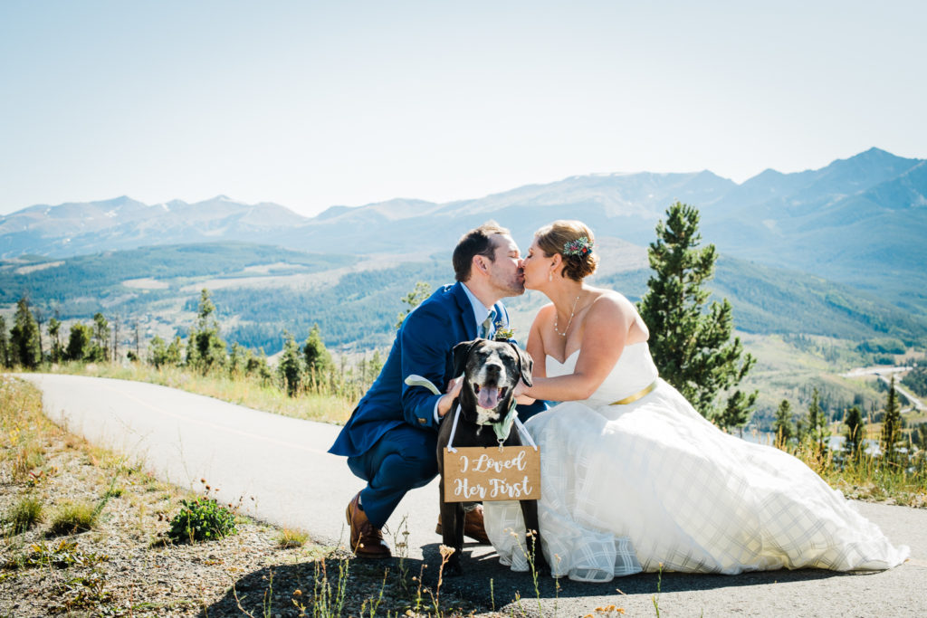 Mountain wedding in Frisco | Groom and bride kiss while they pet dog wearing sign that reads "I loved her first"
