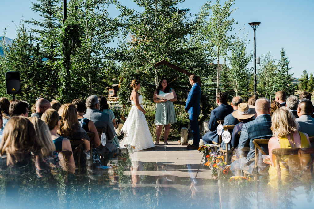 Bride and groom are married by female celebrant while crowd of guests watch