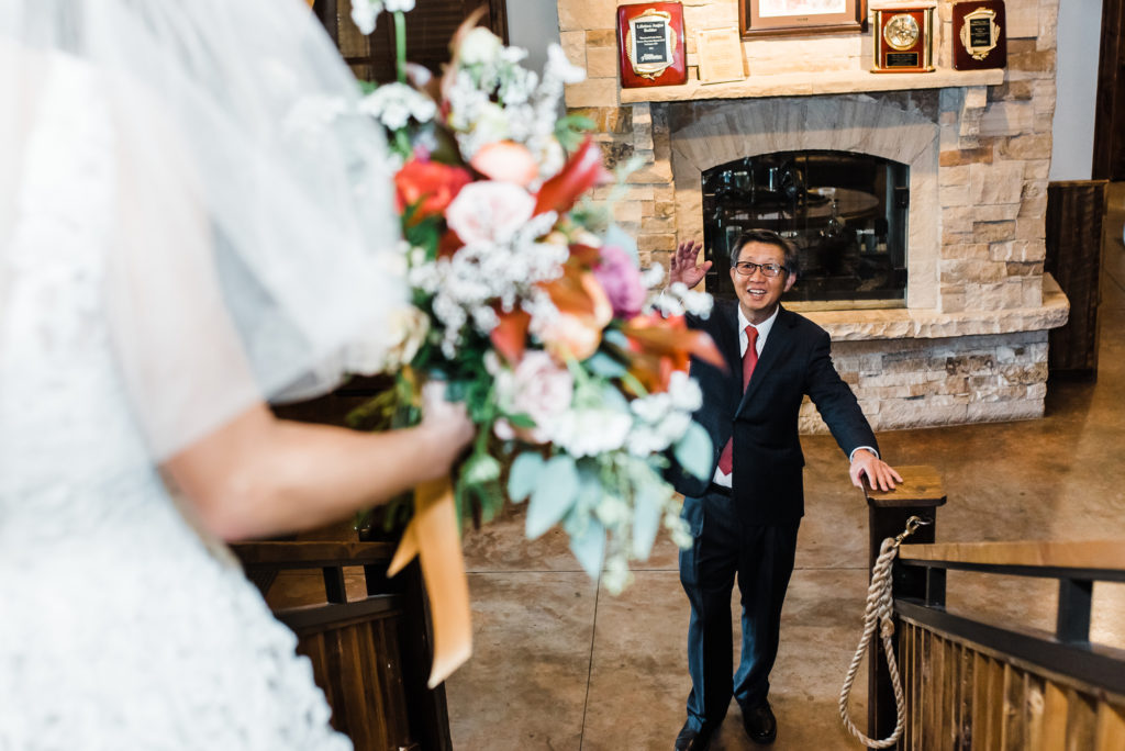 Wedding Photography | Bride descends staircase with bouquet while groom smiles up at her