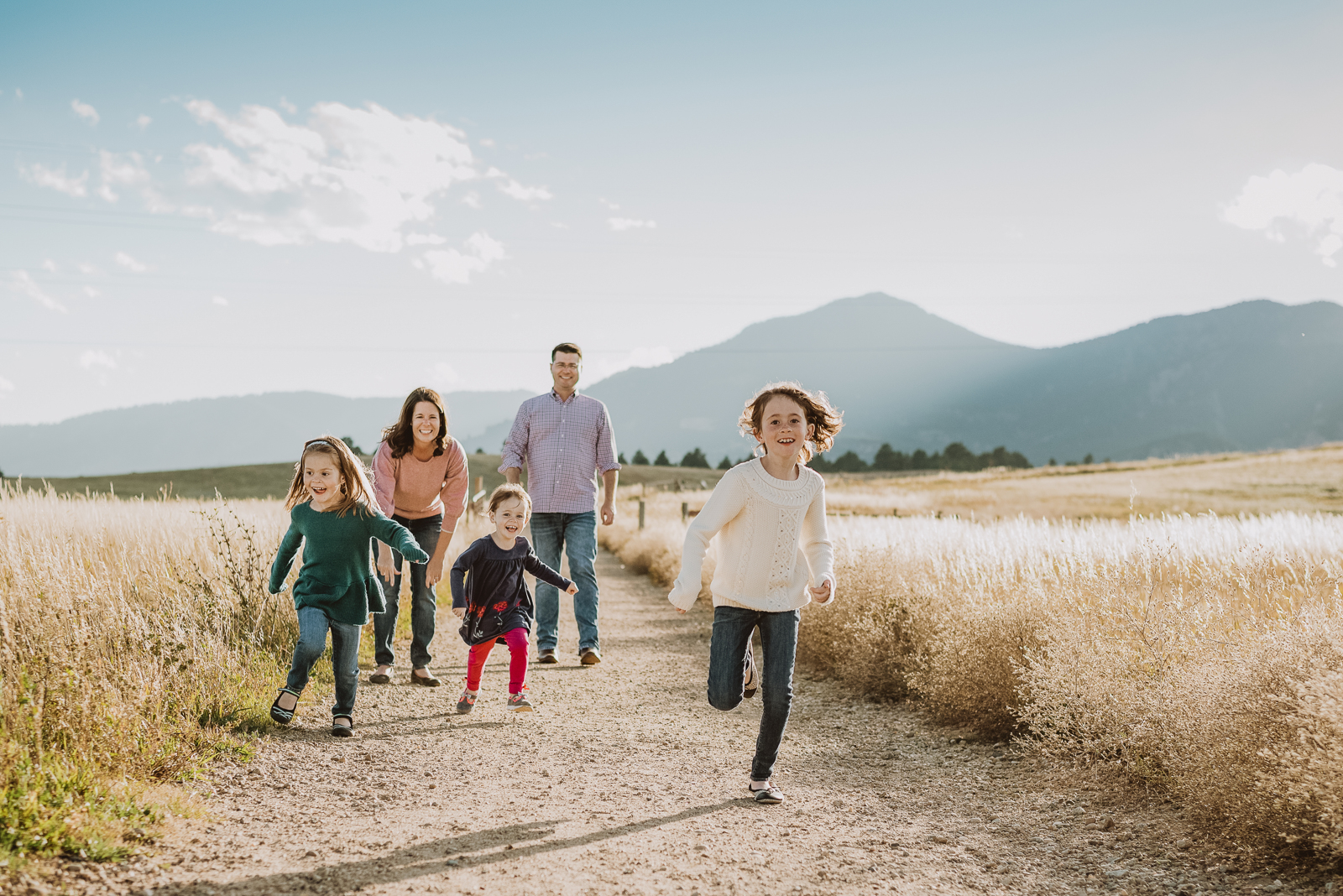 Family group posing together on grassy hillside with mountain backdrop
