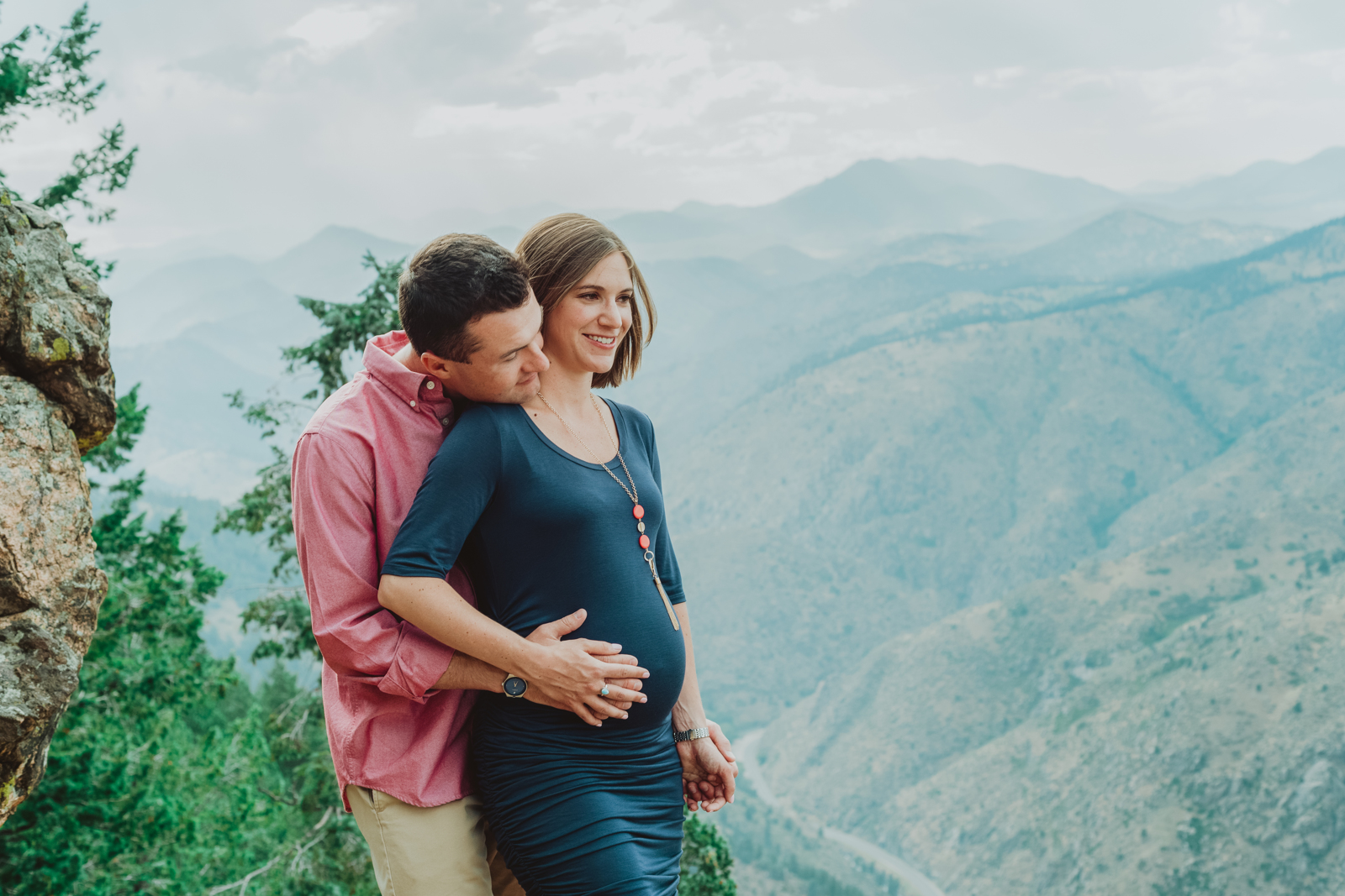 Expectant mother cradling belly with mountains visible in background during maternity session