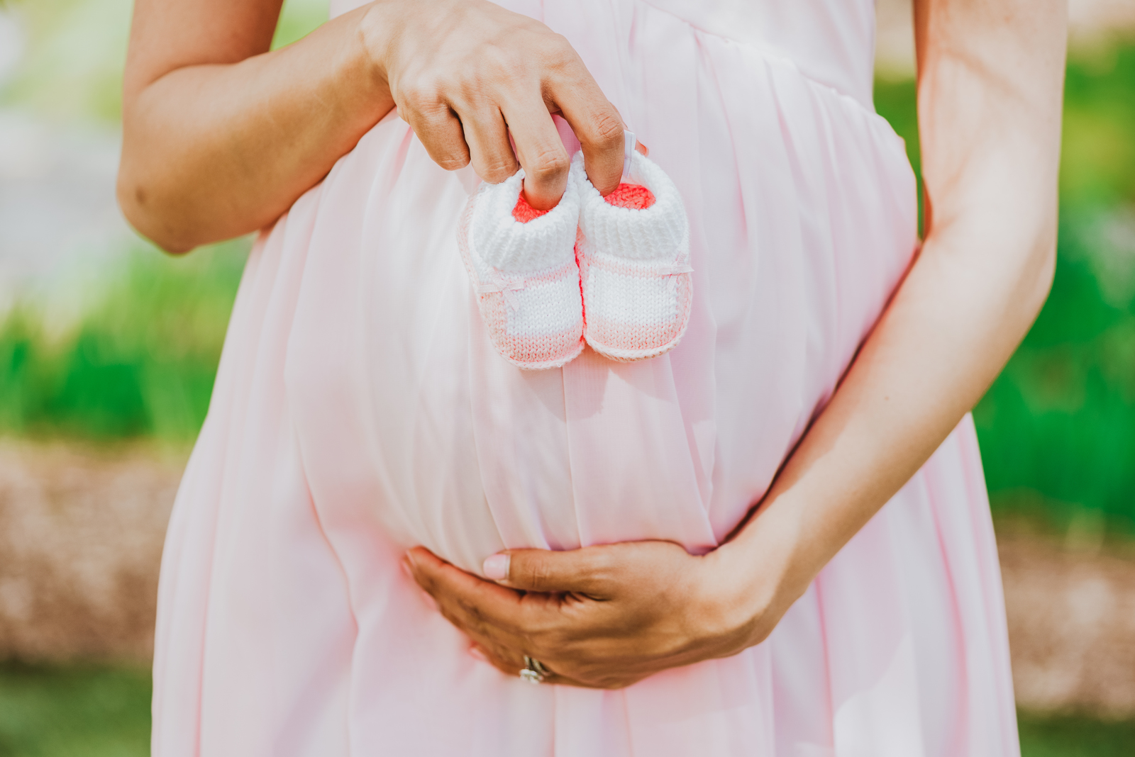 Pregnant woman cradling belly in flowing white maternity gown with blooming garden behind