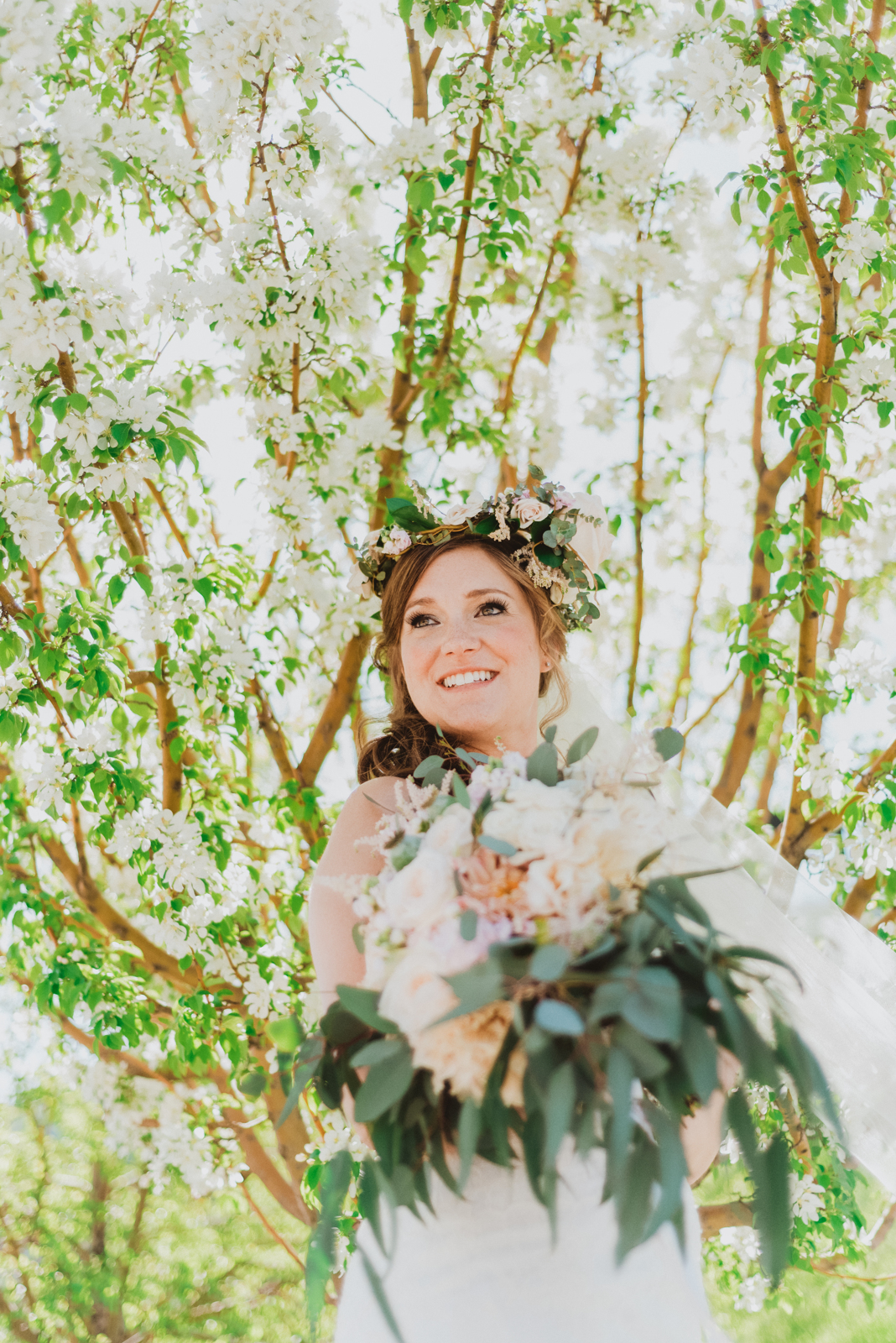 Tall portrait of woman in wedding dress standing in mountain meadow with evergreen forest backdrop