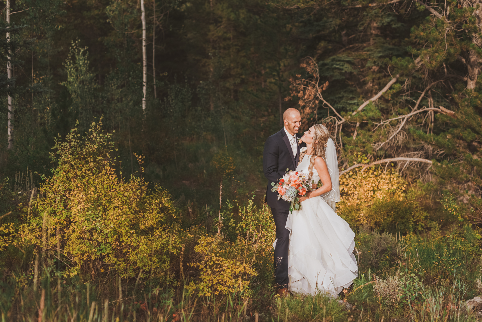 Couple kissing with dramatic mountain scenery and forested slopes behind them in Vail Colorado