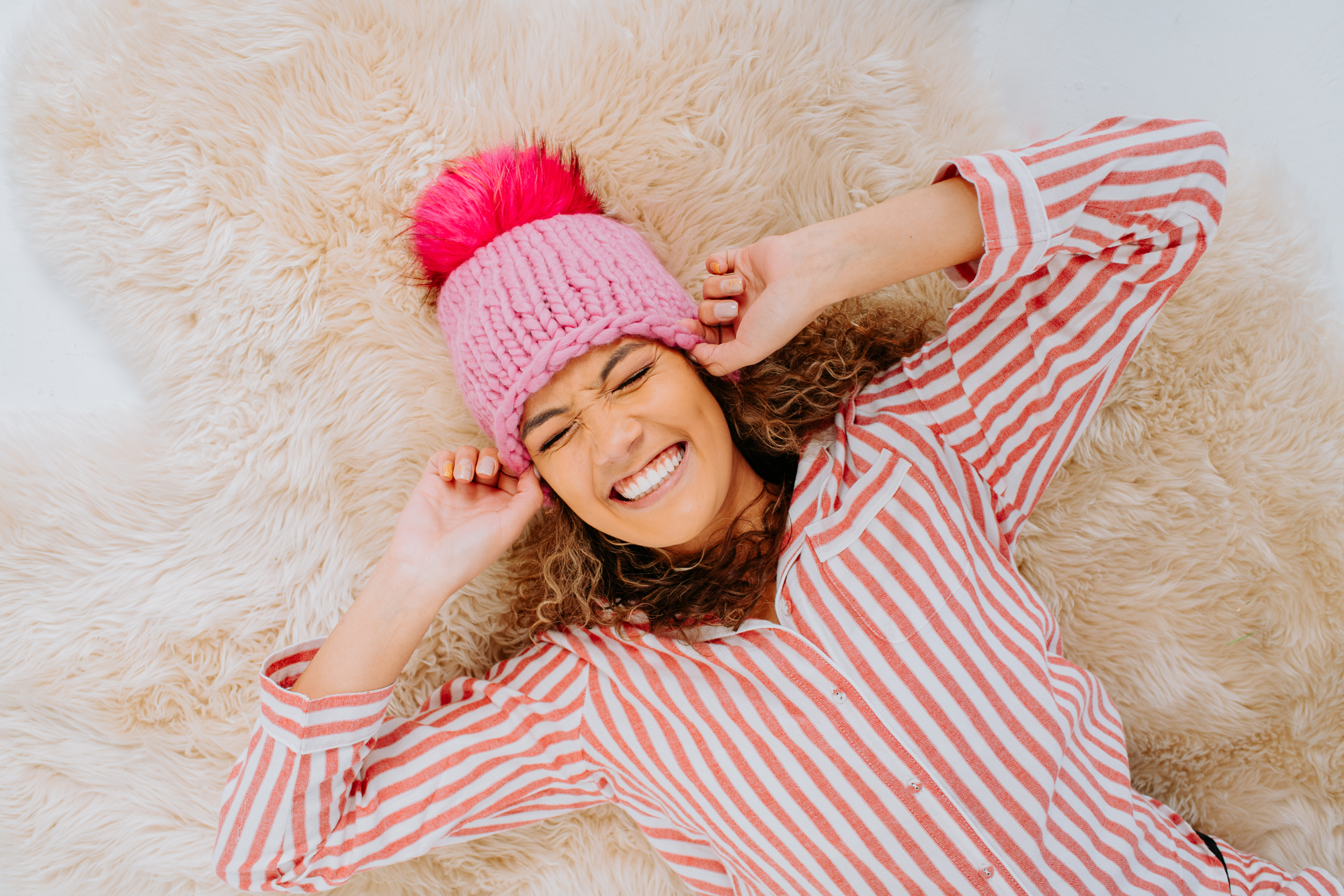 Super G Brand Photography | Smiling model wearing winter hat lies on fluffy carpet | Denver, Colorado