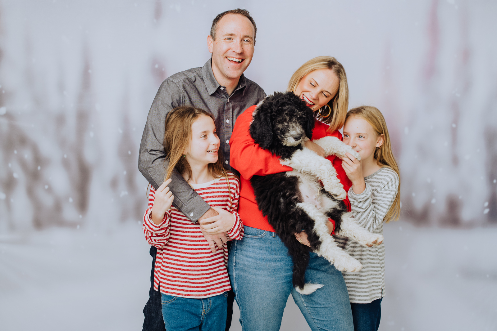 Family bundled together in winter clothing laughing naturally during candid holiday photo session
