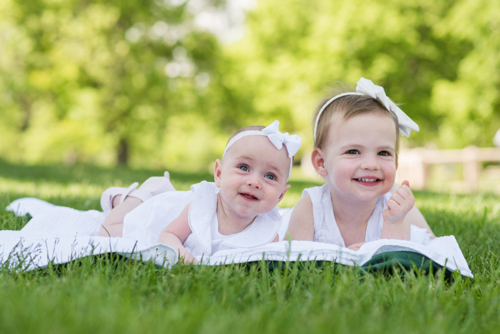 Newborn family photography | sisters on a blanket in the park pose for a photo