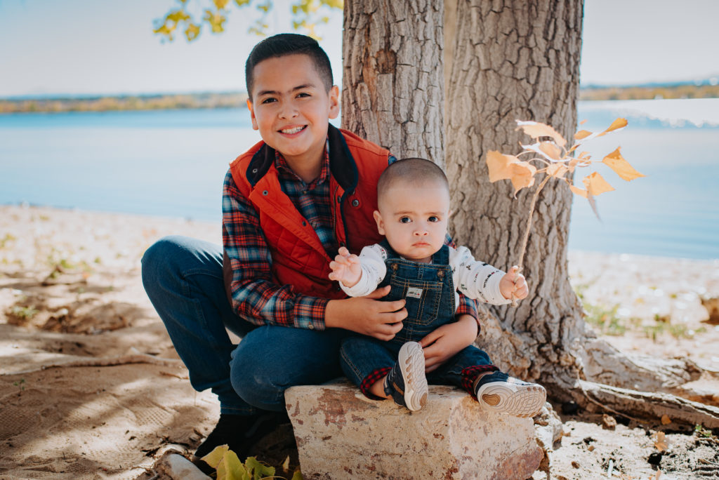Newborn family photography | Siblings pose together with fall autumn leaves in front of a lake