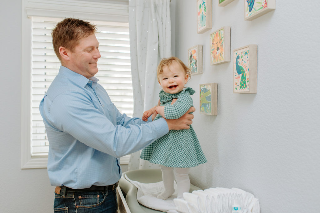 Newborn family photography | Smiling father plays with happy daughter in her nursery