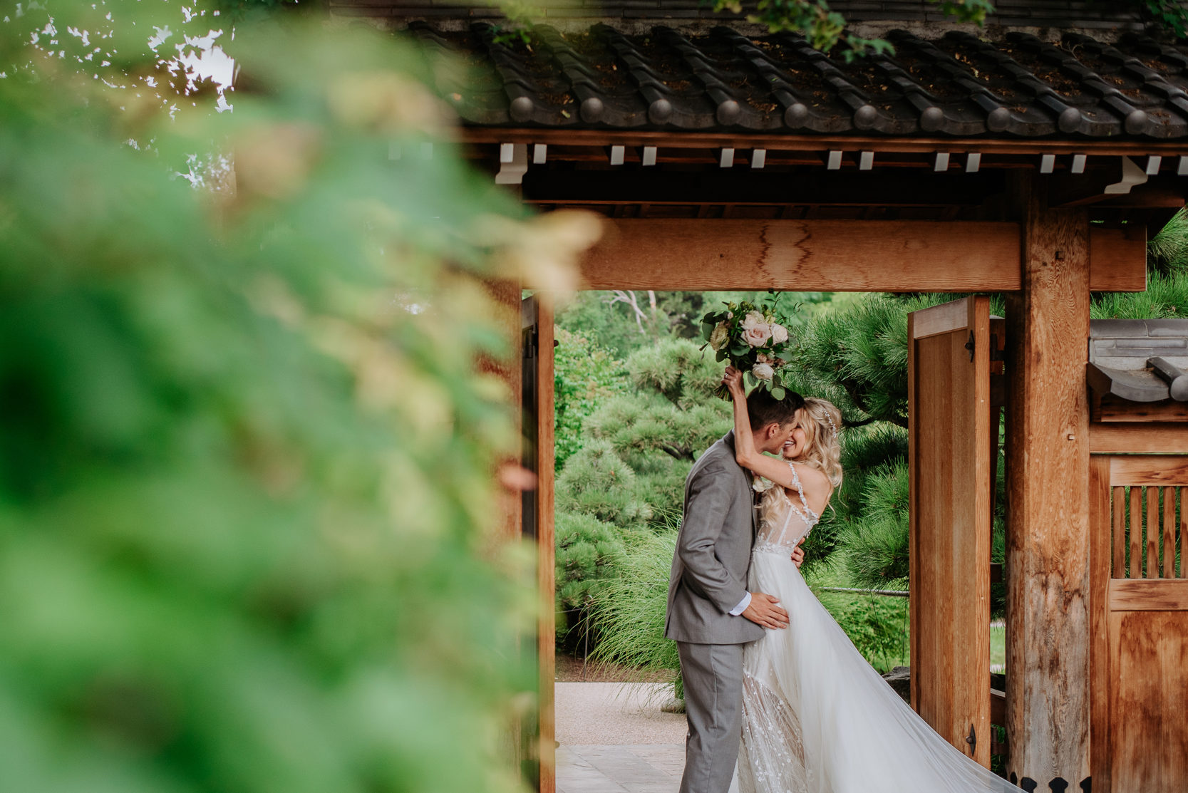 Wedding Photography | Bride and groom kiss beneath gateway | Denver Botanical Gardens