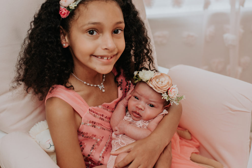 Newborn family photography | Older sister wearing floral crown proudly holds her baby sister in a matching headband for a photo