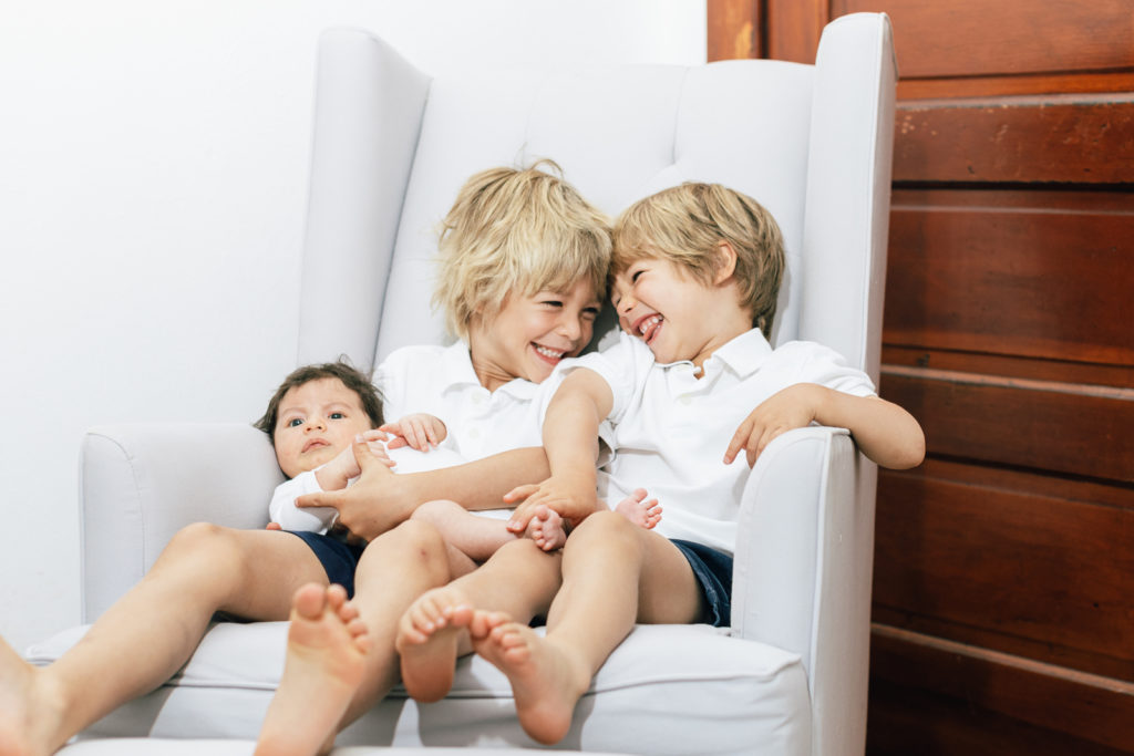 Newborn family photography | Siblings hold and giggle with a new baby sister