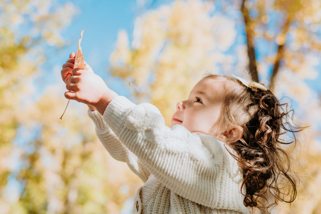 Colorado Fall Family Photo Tips | Child plays with a leaf on a warm fall day with an autumnal sky background