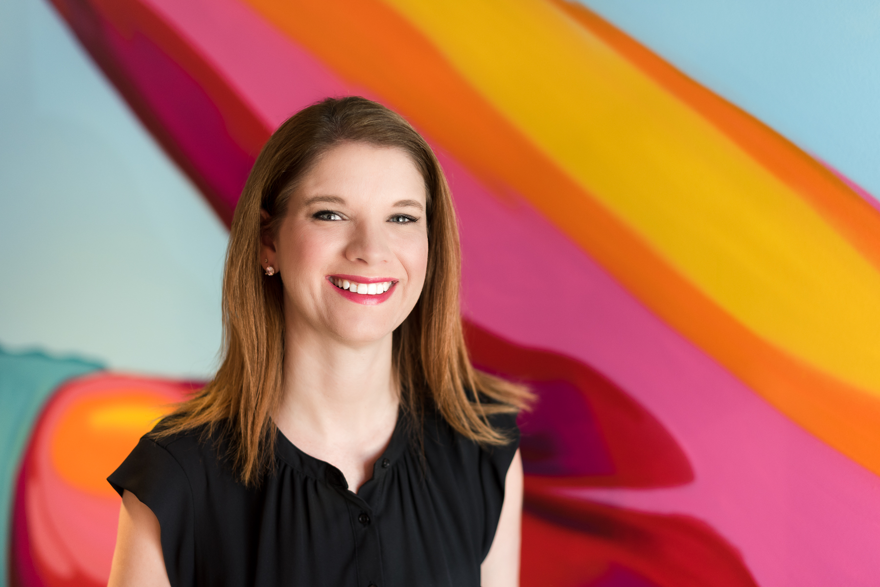 Professional headshot of a woman smiling against a vibrant colorful art background in Denver