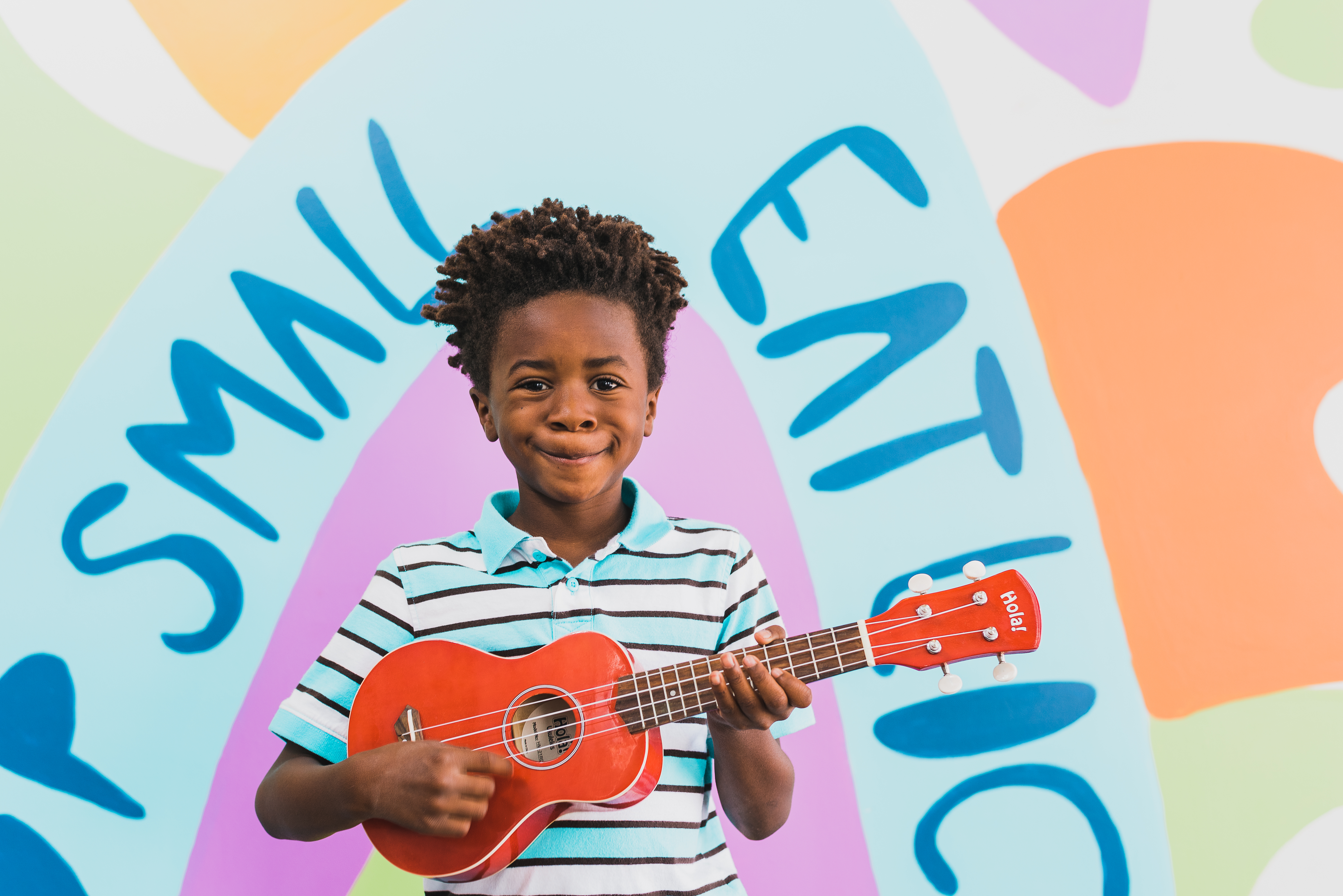 Young musician holding a red guitar in front of a colorful mural wall at Stanley Marketplace in Aurora Colorado