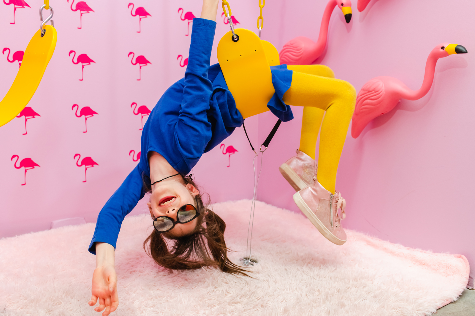 Child swinging joyfully in a pink flamingo themed room at Stanley Marketplace during a creative portrait session