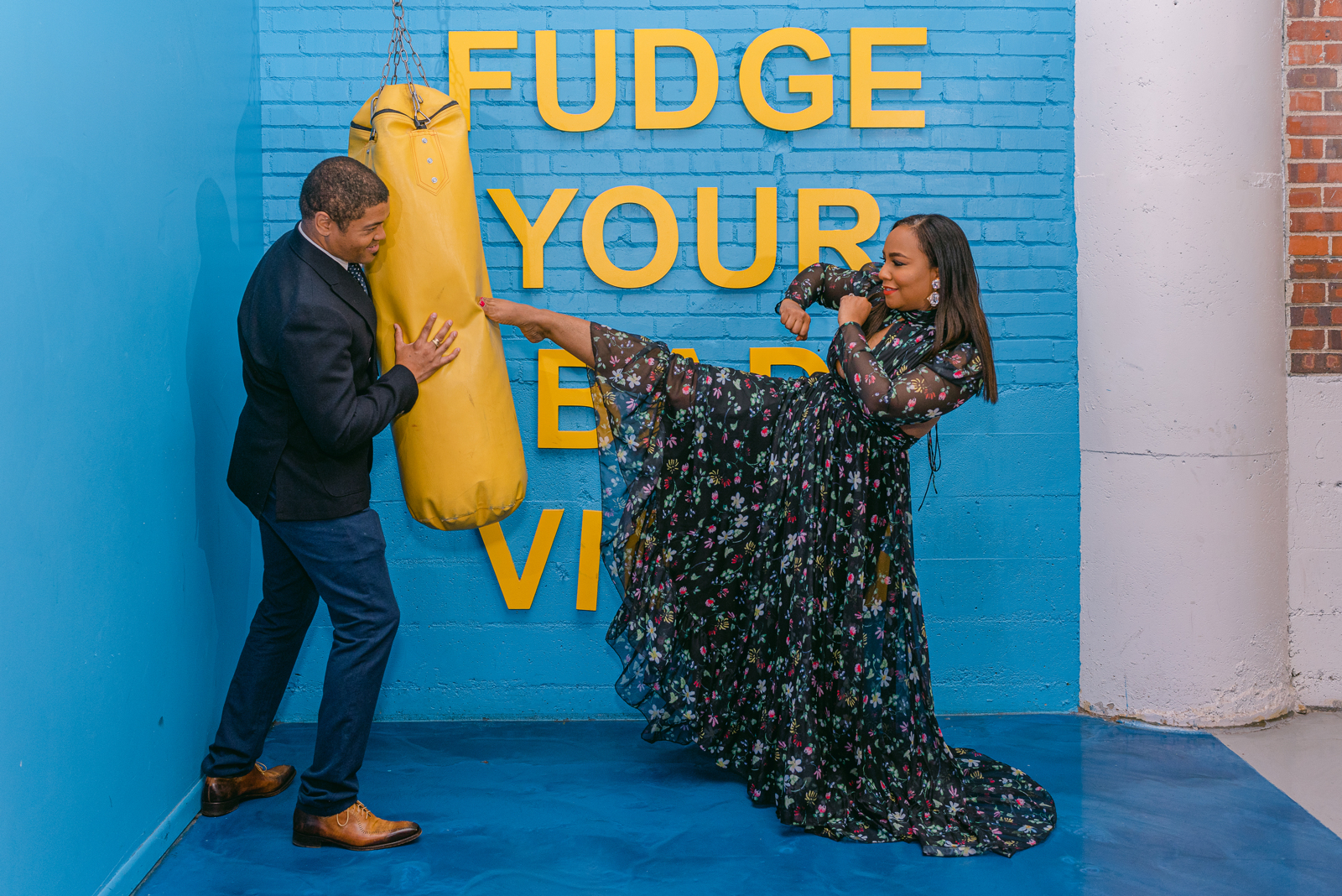 Couple in formal attire striking a playful kickboxing pose at a colorful Denver Selfie Museum backdrop